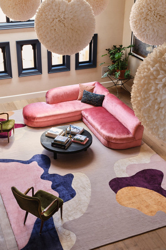 Modern living room with pink sofa, colorful rug, and decorative lights.